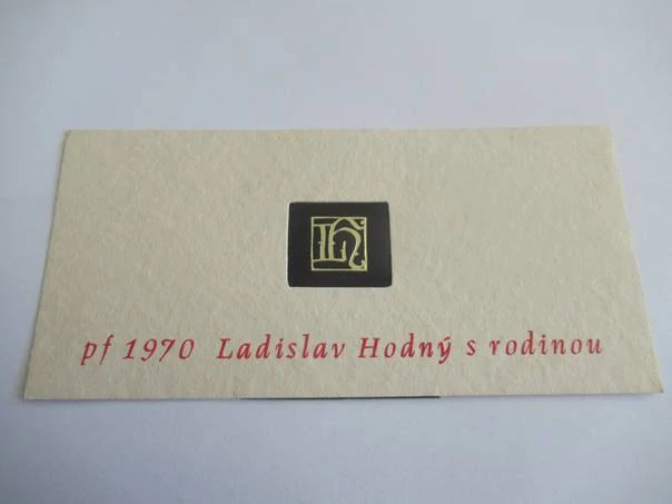 Původní sběratelská novoročenka pf 1970 Ladislav Hodný s rodinou – signet od Oldřicha Menharta, kombinovaná technika, ražený zlatotisk v černém poli (21 × 10 cm)