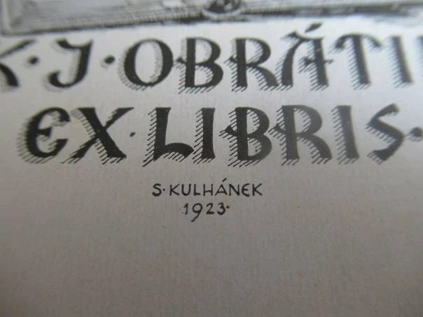 Exlibris – K. J. Obrátil – S. Kulhánek – motiv: Putto otáčející listy obří knihy před historickým portálem s nápisem Uč se moudrým býti – rozměry 10×7,5 cm – zinkové klišé / pérovka (P1) – rok 1923